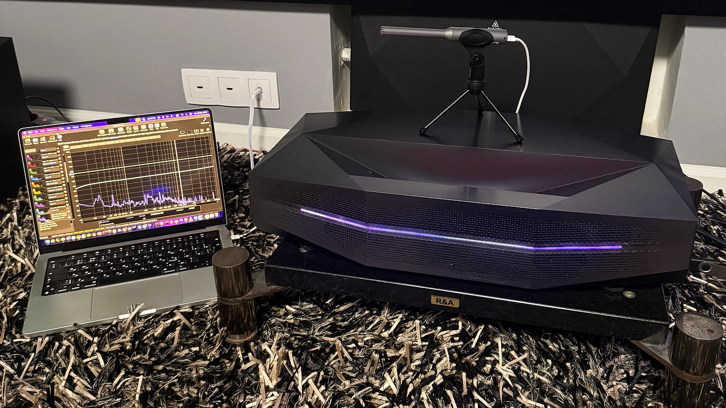 A calibrated UMIK-1 microphone on the projector chassis, with the spectrum recorded in REW on a laptop